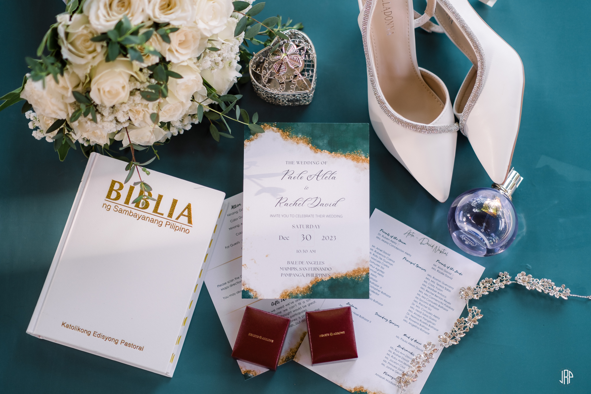 Wedding flat lay featuring invitation, Bible, bridal shoes, bouquet, and jewelry boxes